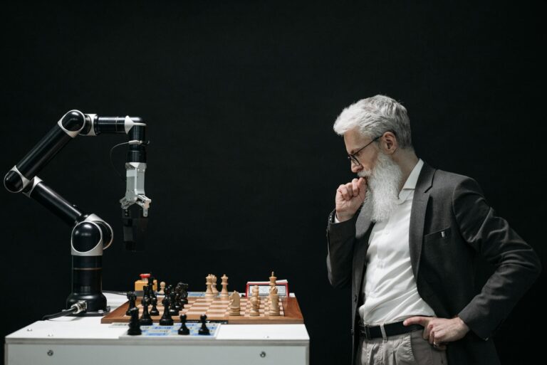 An elderly scientist contemplates a chess move against a robotic arm on a chessboard. US Government/Artificial Intelligence