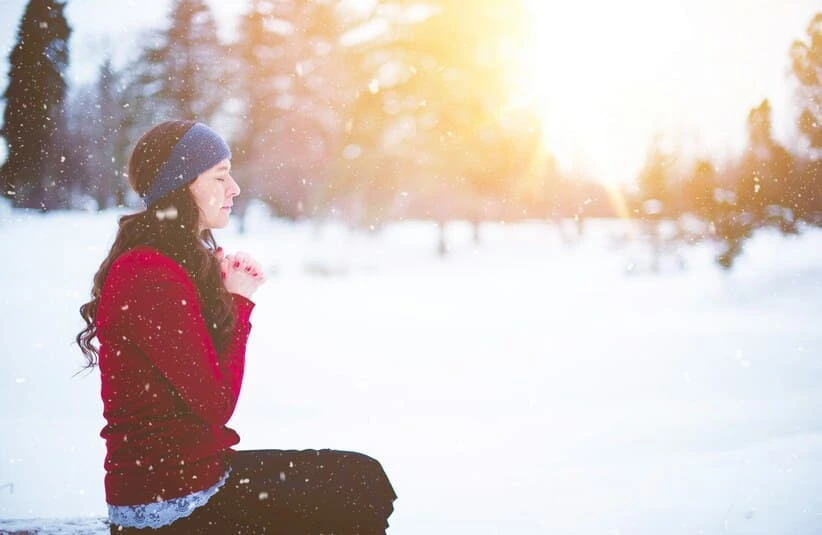 Woman in red praying in a snowy landscape. 