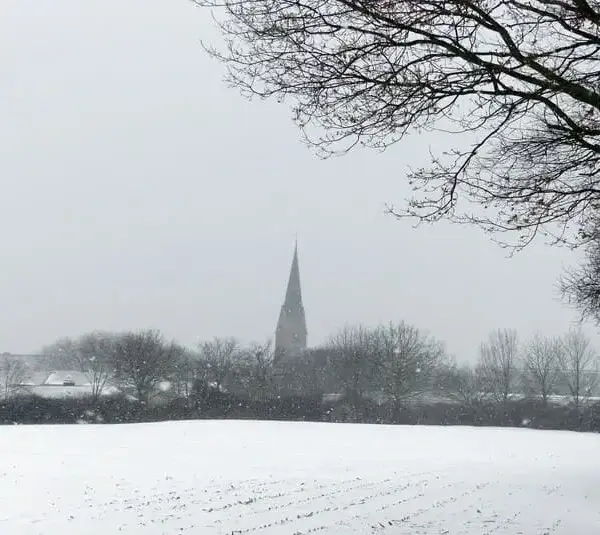 A snowy field with a church steeple in the distance. Solitude in winter.