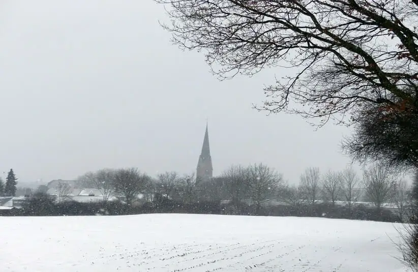 A snowy field with a church steeple in the distance. Solitude in winter.