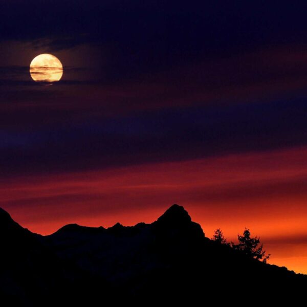 A captivating scene of a full moon above silhouetted mountain peaks against a vivid sunset sky. manifesting, Taurus Full Moon