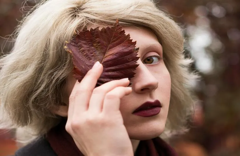 person covering their face with a leaf wearing dark lipstick perfect choice for a good fall lip color. fall beauty