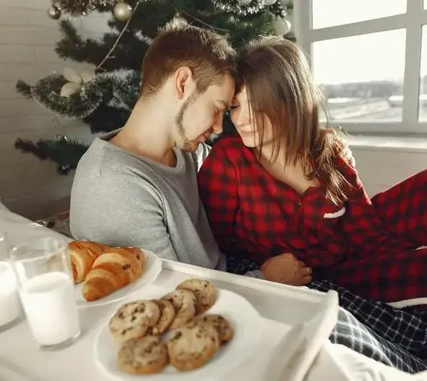 A couple sitting in front of a Christmas tree. Working to find ways to focus on romance during the busy holiday season.