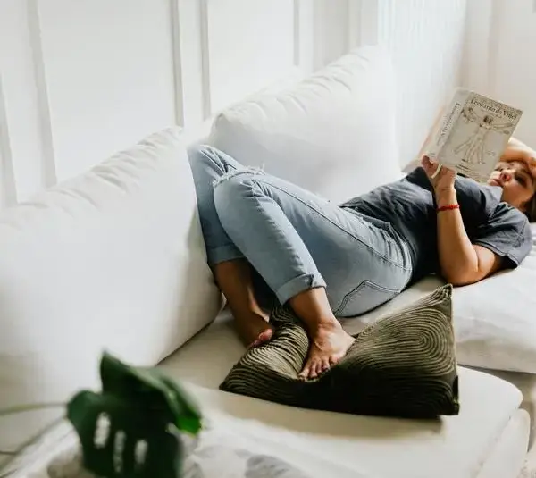 A woman reading a book on the couch. This can be a good way to rest for your mental health during the holiday season.