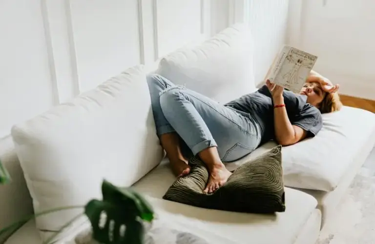 A woman reading a book on the couch. This can be a good way to rest for your mental health during the holiday season.