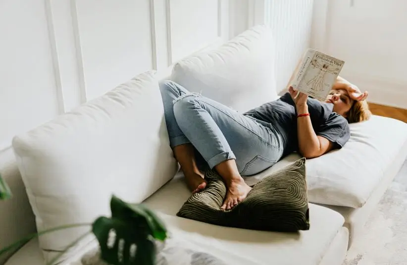 A woman reading a book on the couch. This can be a good way to rest for your mental health during the holiday season.