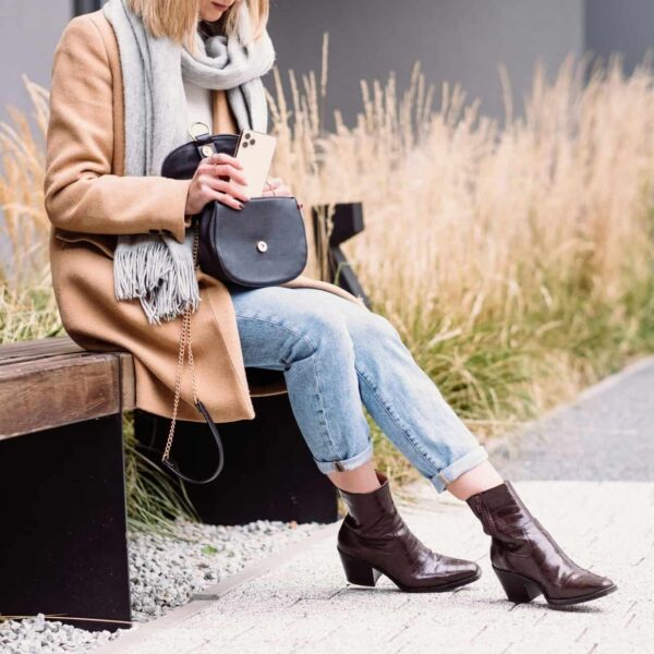 Elegant woman in a coat and scarf using her phone on a bench outdoors in Warsaw. fall boots