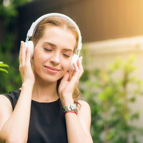 Smiling woman listening to music new single with headphones in sunny garden setting.