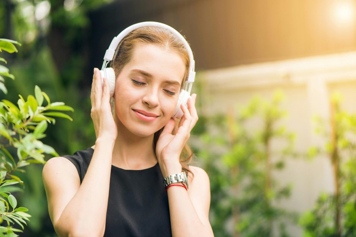 Smiling woman listening to music new single with headphones in sunny garden setting.