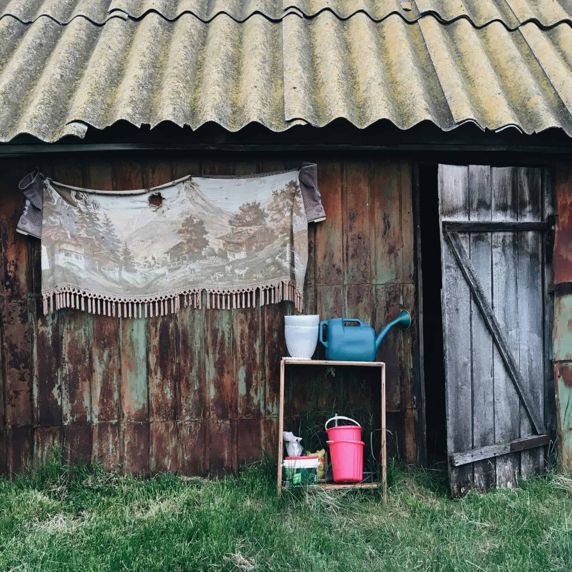 A rustic barn exterior with a weathered door and gardening tools on a wooden shelf.