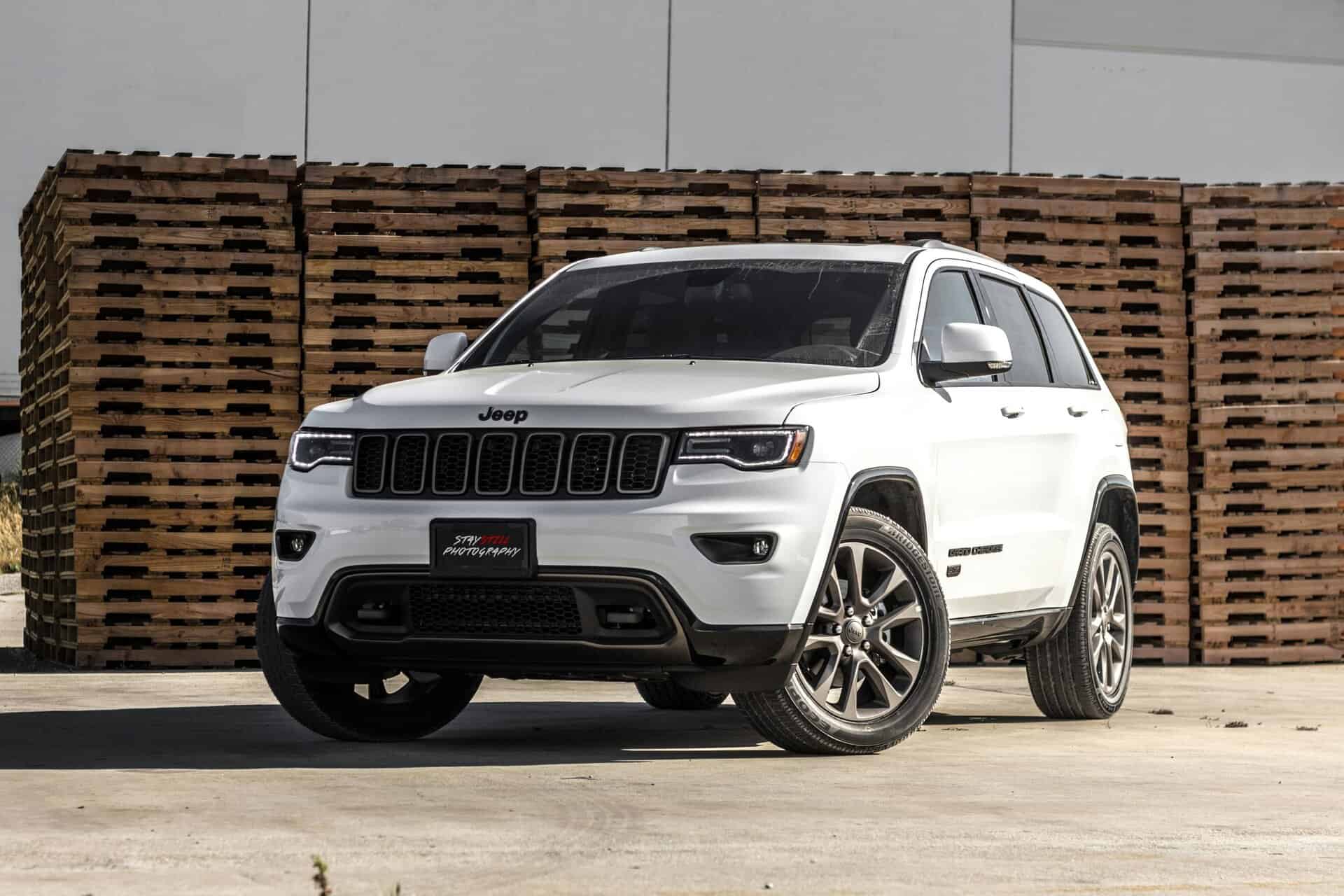 A sleek white Jeep Grand Cherokee parked in front of stacked wooden pallets, showcasing its luxury features.