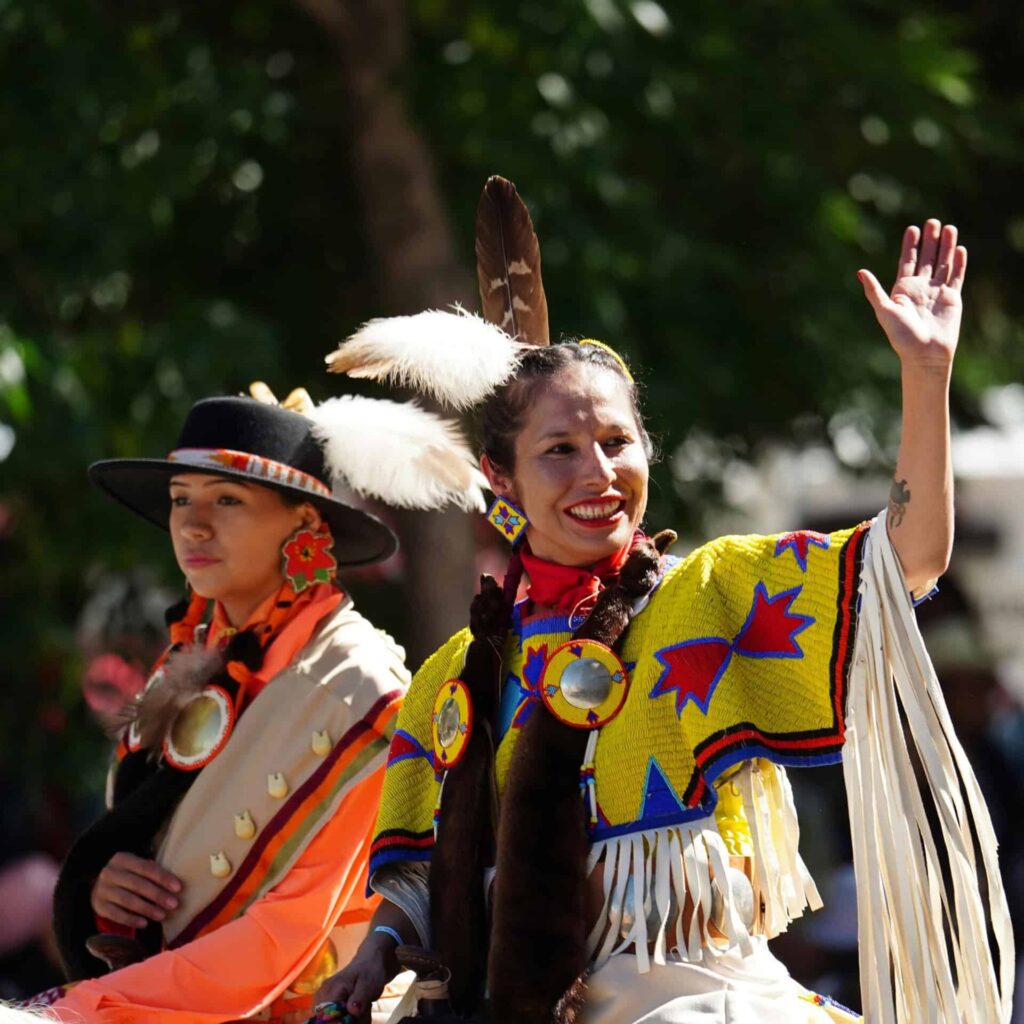Smiling Native American women in vibrant traditional costumes celebrating outdoors., Indigenous