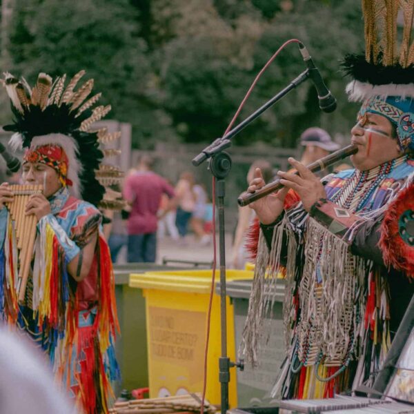 Native American musicians performing outdoors in traditional wear with woodwind instruments.