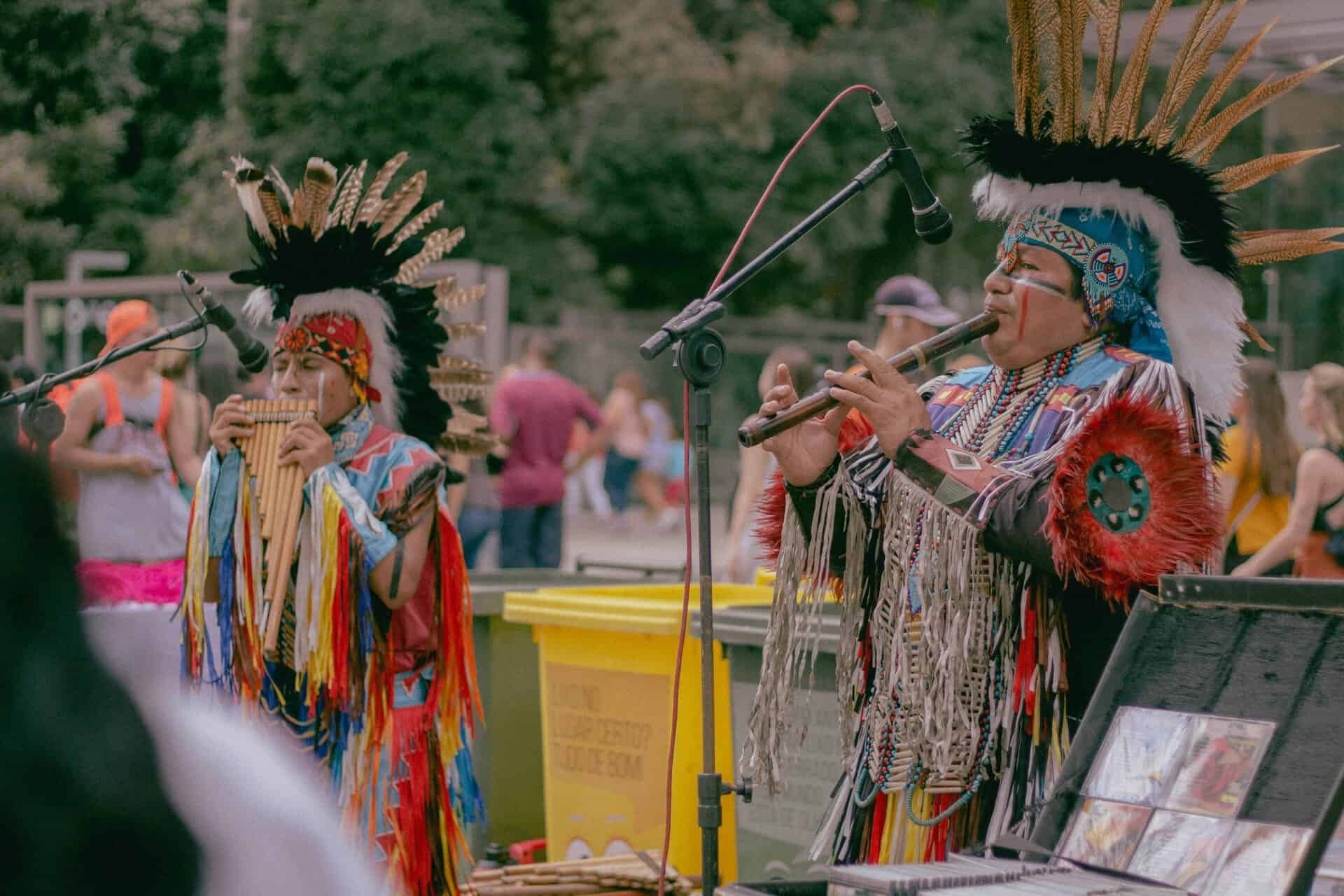 Native American musicians performing outdoors in traditional wear with woodwind instruments.