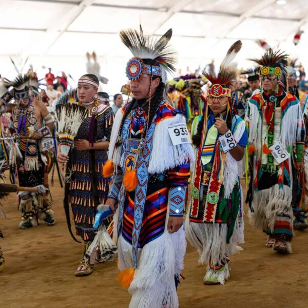 Native American dancers in colorful traditional attire at a vibrant pow wow gathering. Native American Designers