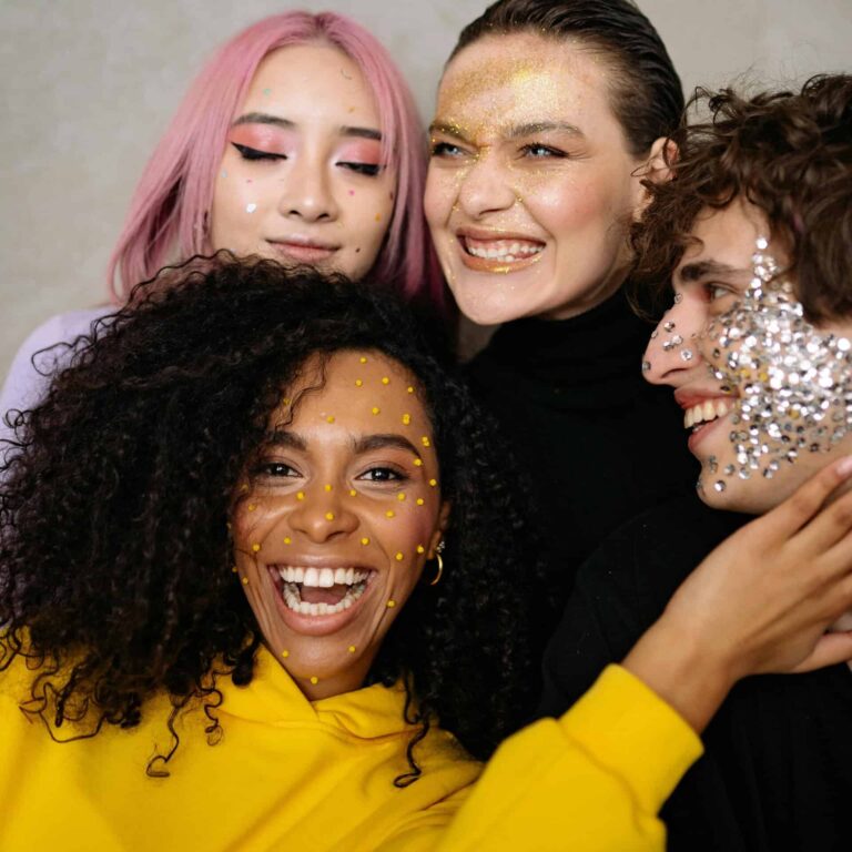 Joyful group of Gen Z friends with colorful glitter makeup, celebrating diversity and style in a close-up studio portrait, celebrating Friendsgiving with no stresses.