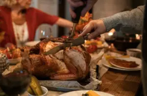 person slicing a turkey surrounded by people for the holiday