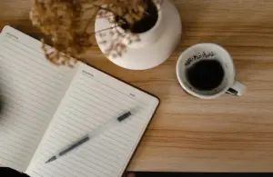 A journal or notebook, cup of coffee, and flowers, on a desk. spiritual decluttering