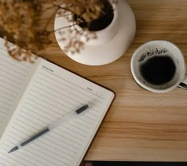 A journal or notebook, cup of coffee, and flowers, on a desk. spiritual decluttering