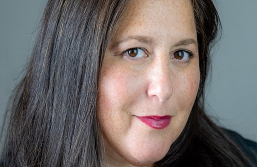 Sundance Comms Head Tammie Rosen, with long dark hair and light makeup, including red lipstick, gazes confidently at the camera. The background is a neutral gray, creating a professional tone.