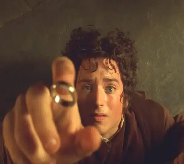 Frodo Baggins, from "The Lord of the Rings: The Fellowship of the Ring," reaches toward a hovering gold ring with a determined expression. The scene conveys tension and focus. Stone floor background.
