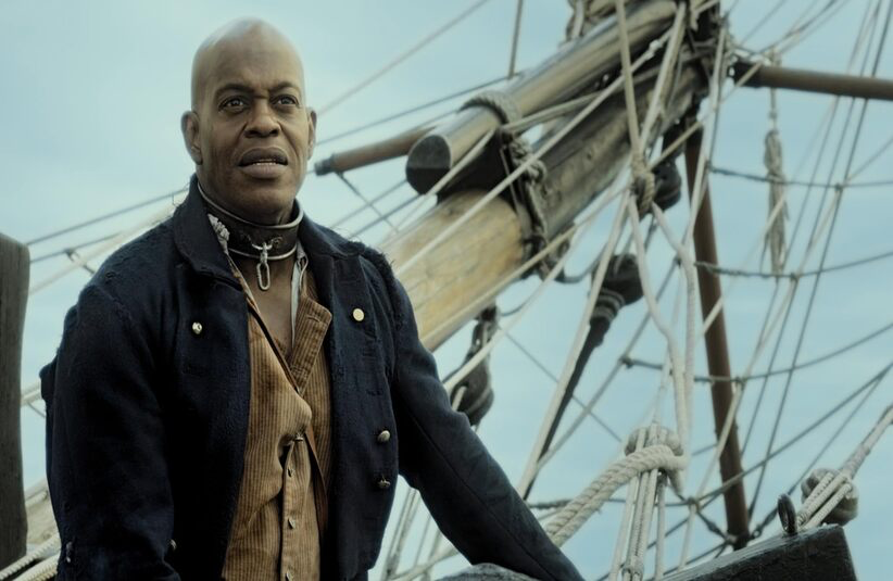 Jubilant Sykes in historical attire stands confidently on a ship's deck, with ropes and wooden masts in the background against a clear sky. The mood is determined.