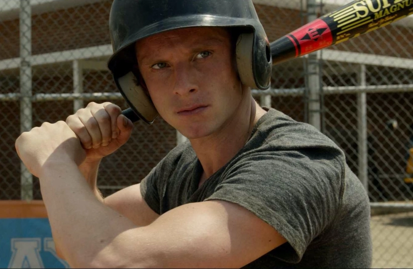 A person wearing a black helmet and gray shirt is holding a baseball bat, ready to swing. They appear focused and determined, standing in front of a chain-link fence.