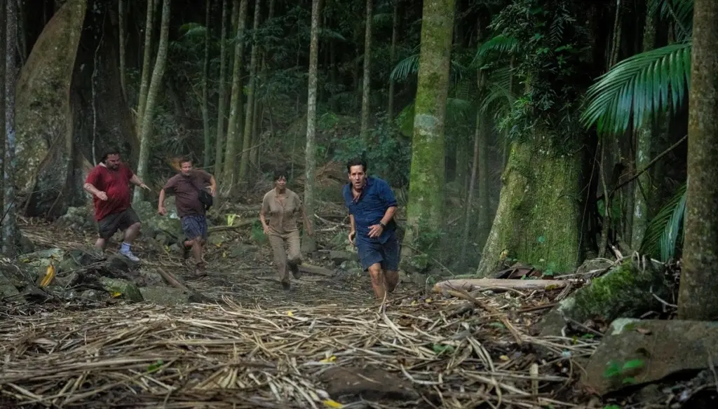 Four people run through a dense, misty forest with tall trees and scattered leaves. They appear focused and determined, evoking tension and urgency.