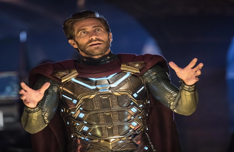 Man in an ornate, glowing armored suit with a maroon cape gestures dramatically. He appears intense and focused, set against a dimly lit background.