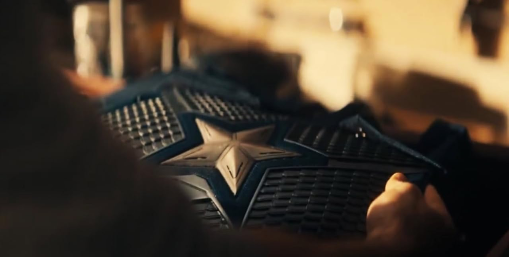 Close-up of a person holding a dark blue, textured armor with a prominent silver star in the center. The lighting is warm, creating a dramatic and focused atmosphere.