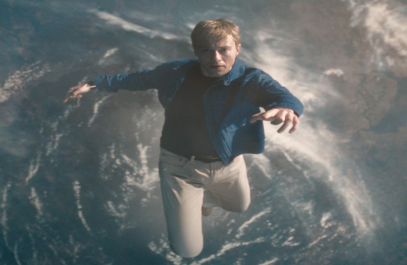 A man in a blue jacket and white pants appears to be floating or falling through space, with Earth visible below. The scene conveys a sense of wonder and surrealism.