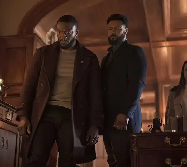 Aldis Hodge, Alona Tal, and Isaiah Mustafa in "Cross (2024)" stand pensively in an elegant, wood-paneled room with ornate decor. The atmosphere is tense, hinting at a serious or dramatic moment.