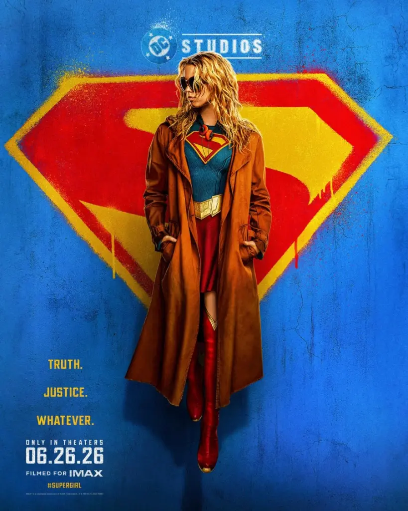 Blonde woman in Supergirl costume and brown coat stands confidently against a large red and yellow Superman symbol on a blue wall. Text reads "Truth. Justice. Whatever. Only in Theaters 06.26.26. Filmed for IMAX."