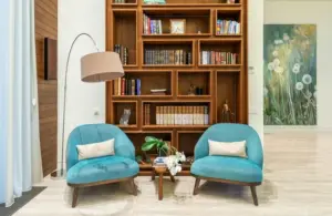 A reading nook with a floor lamp, 2 chairs, a small table, and a bookshelf behind