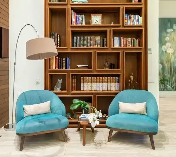 A reading nook with a floor lamp, 2 chairs, a small table, and a bookshelf behind