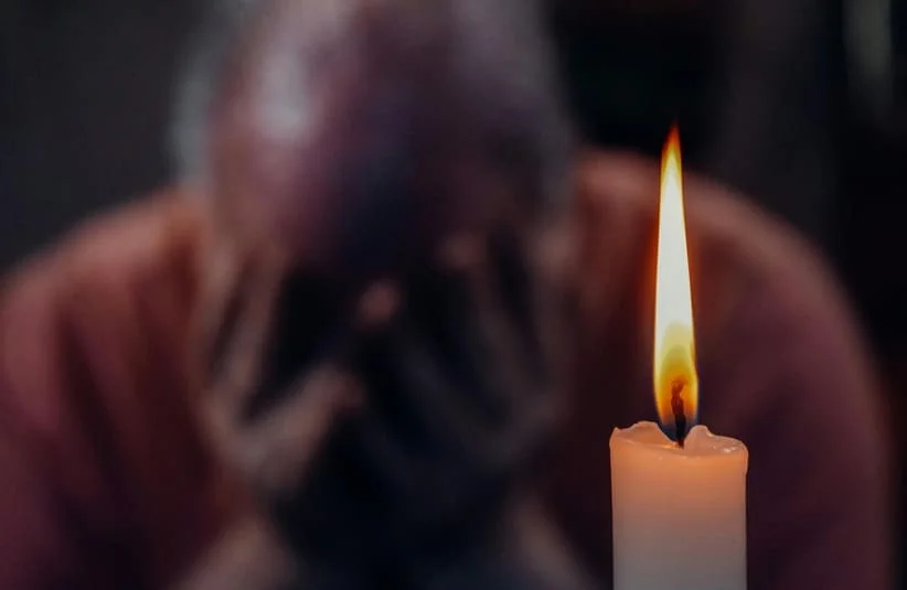 Image of a blurred man in the background, mourning, crying while a lite candle sits in front of him, grief during the hoildays