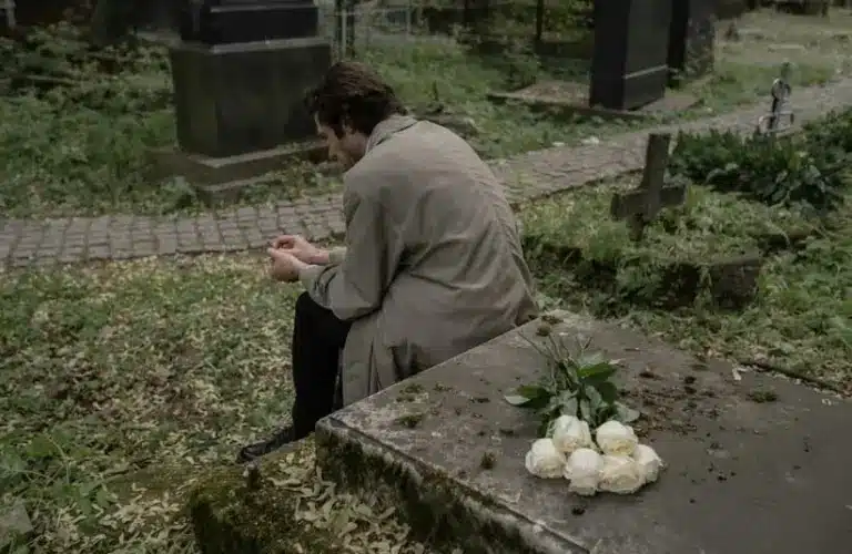 Man sitting on a grave, mourning the lost of a loved one, grief, holidays, coping methods