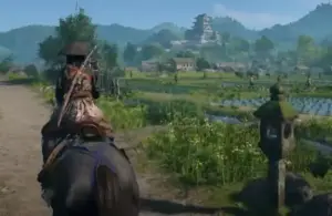 Assassin's Creed Shadows samurai rides on a horse down a rural path, surrounded by lush fields and distant mountains.