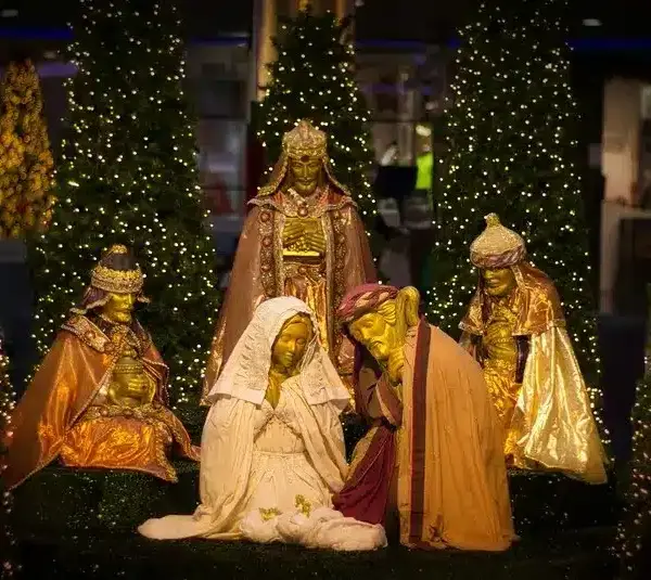 A warm, glowing nativity scene with Mary, Joseph, the Wise Men, and Christmas trees illuminated by festive lights., We Three Kings