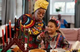 Photo of a woman and child lighting candles of a Kwanzaa kinara