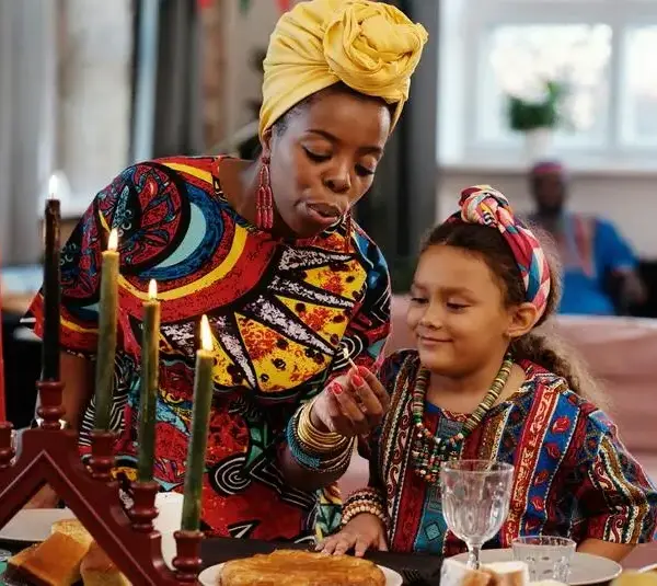 Photo of a woman and child lighting candles of a Kwanzaa kinara