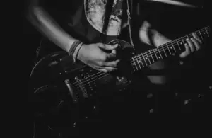 Black and white close-up of a person playing an electric guitar, focusing on their hands and guitar. The scene conveys an intense, passionate musical rock album vibe from 2025.