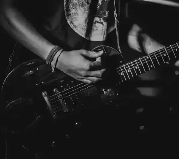 Black and white close-up of a person playing an electric guitar, focusing on their hands and guitar. The scene conveys an intense, passionate musical rock album vibe from 2025.