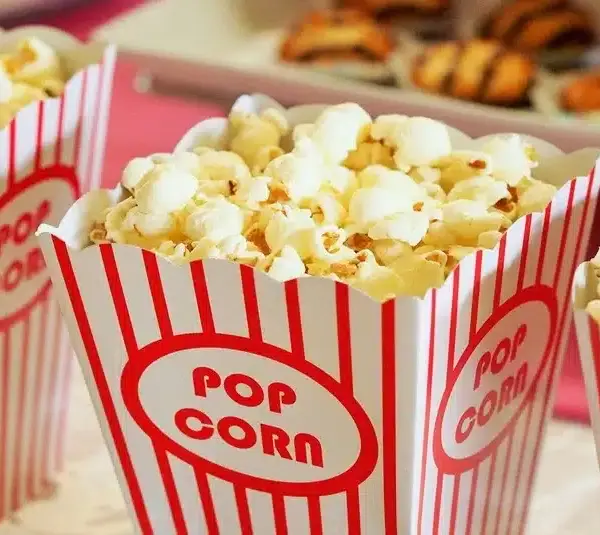 Three striped popcorn containers filled with freshly popped corn are in the foreground. The scene is light-hearted, evoking a movie night ambiance. Disney.