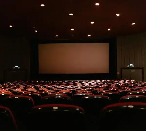 Empty movie theater with rows of red seats facing a large blank screen. Soft ceiling lights create a calm, expectant atmosphere.
