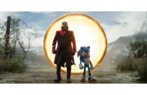 A blue anthropomorphic hedgehog and a man in a black and red coat stand on a dirt road near a glowing golden ring. Mountains and cloudy sky are in the background. Dr. Robotnik (portrayed by Jim Carrey) and Sonic,(portrayed by Ben Schwarz) Courtesy of Paramount Pictures and Sega of America, Inc.