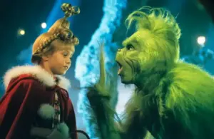 Taylor Momsen, plays young girl with an elaborate hairstyle and red coat faces a green, Jim Carrey, a furry creature gesturing animatedly. The scene is colorful and whimsical, getting ready to The Pretty Reckless rendition of her song in "How the Grinch Stole Christmas," 2000.