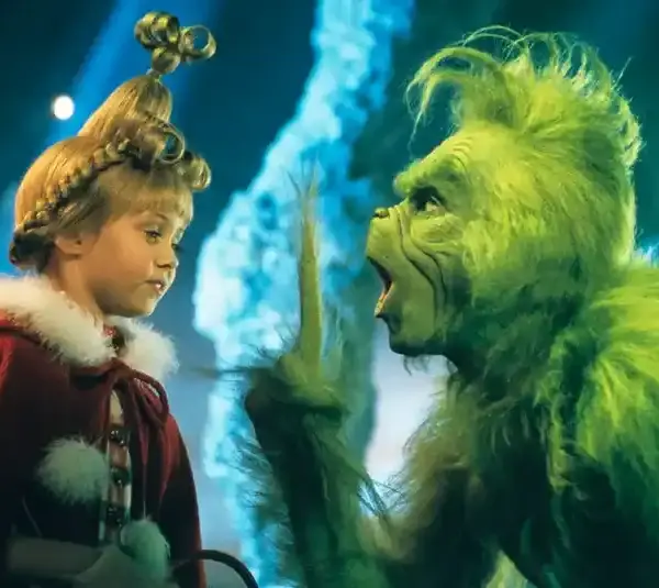 Taylor Momsen, plays young girl with an elaborate hairstyle and red coat faces a green, Jim Carrey, a furry creature gesturing animatedly. The scene is colorful and whimsical, getting ready to The Pretty Reckless rendition of her song in "How the Grinch Stole Christmas," 2000.