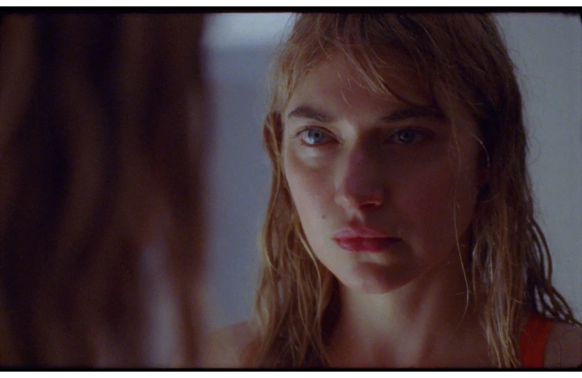 Imogen Poots, with wet hair and a calm expression, gazes intently at her reflection in a mirror. The lighting is soft, creating a contemplative mood.
