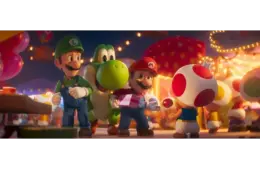 Mario, Luigi, Yoshi, and Toad joyfully walk through a festive, brightly lit market. Mario holds a gift, while Toad offers a red lollipop in The Super Mario Galaxy Movie